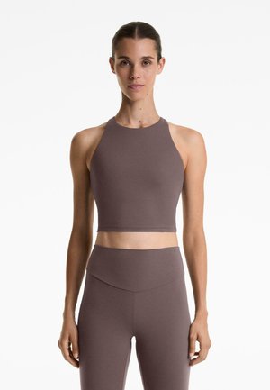 Crop top in a muted mauve color, made of smooth material with a high neckline and wide shoulder straps. Paired with high-waisted leggings.