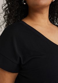 Top nero a V con maniche corte, realizzato in tessuto liscio. Presenta una vestibilità comoda e una leggera lucentezza sul materiale.