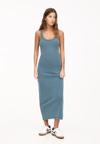 Rochie maxi ajustată, fără mâneci, de culoare teal, cu decolteu rotund și slituri laterale, asociată cu pantofi sport albi și negri.