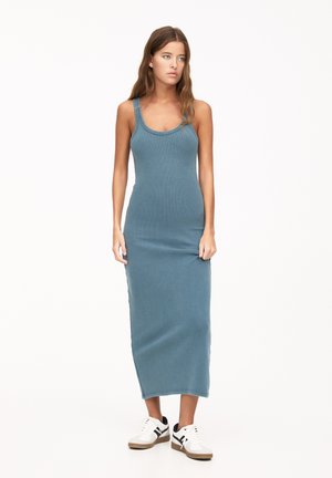 Form-fitting, sleeveless, teal maxi dress with a round neckline and side slits, paired with white and black athletic shoes.