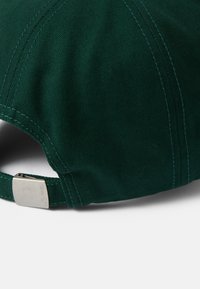 Berretto verde scuro con visiera curvata, realizzato in tessuto resistente. Presenta una cucitura a contrasto e una fibbia regolabile in argento sul retro.