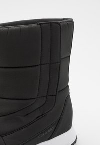 Botas negras aisladas con un diseño acolchado, textura suave y una suela exterior blanca contrastante. Marca COLD RDY en el costado.
