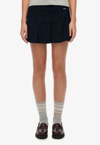 Gonna a righe blu navy con pieghe, abbinata a calze a righe grigie e beige e mocassini bordeaux. Tessuto liscio con una vestibilità sartoriale.