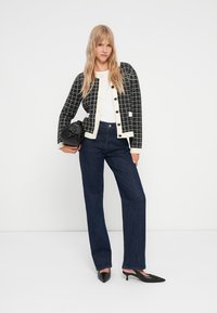 Μαύρο και άσπρο κομμένο μπολερό πάνω από λευκή μπλούζα, συνδυασμένο με σκούρα μπ�λε φαρδιά τζιν και μαύρες μυτερές γόβες. Μαύρη τσάντα.