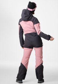 Tuta da sci in rosa e grigio scuro, caratterizzata da un cappuccio, design aderente, pannelli a contrasto e tasche con zip, realizzata in materiale impermeabile.