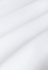 Närbild av slät vit tyg med synlig fin vävstruktur och mjuka veck.