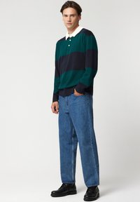 Zielono-granatowa, paskowana polo z dzianiny, z białym kołnierzykiem. Połączona ze jasnoniebieskimi jeansami o prostym kroju i czarnymi sznurowanymi butami.