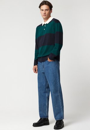 Zielono-granatowa, paskowana polo z dzianiny, z białym kołnierzykiem. Połączona ze jasnoniebieskimi jeansami o prostym kroju i czarnymi sznurowanymi butami.