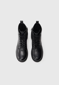 Mustad mustad nahast pahklu saabaste paelad ees, külgsel lukul, ümar varvas ja sile tekstuur. Õmmeldud detailid äärel.