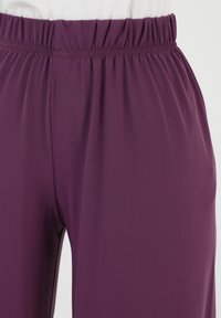 Paarse rekbare broek met een elastische tailleband en soepele textuur, met een ontspannen pasvorm zonder zichtbare sluitingen of patronen.