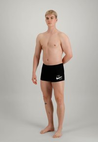 Shorts de bain noirs avec le logo blanc de Nike sur le côté gauche, design ajusté, fabriqués en matériau lisse et extensible.
