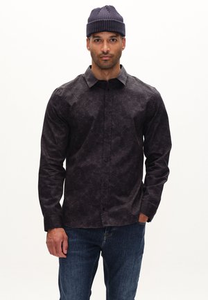 Dark patterned button-up shirt with a collar and long sleeves, made from textured fabric; worn with blue jeans and a navy knit beanie.
