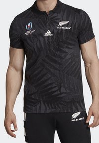 Svart pikétröja med fjädrande mönster, som har VM- och All Blacks-logotyper, adidas-märke och klassisk krage. Kortärmad.