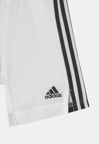Białe sportowe spodenki wykonane z gładkiego materiału, z trzema czarnymi paskami po bokach i małym czarnym logo Adidas na hemie.
