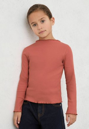 Top met lange mouwen in geribd, roestoranje stof, met een golvende kraag en zoom, gecombineerd met donkere jeans.