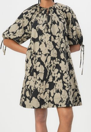 Robe noire ample avec motif floral beige, manches bouffantes longueur coude et détails à nouer au niveau de l'encolure et aux extrémités des manches.