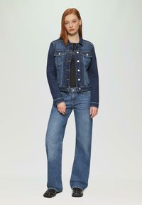 Donkerblauwe denimjack met borstzakken, zilveren hardware en contrasterende stiksels. Gecombineerd met lichtblauwe wijde jeans.