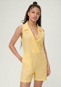Geel linnen jumpsuit met een uitgesneden kraag, korte mouwen en zijzakken. Gladde textuur, getailleerd ontwerp en relaxed shorts.