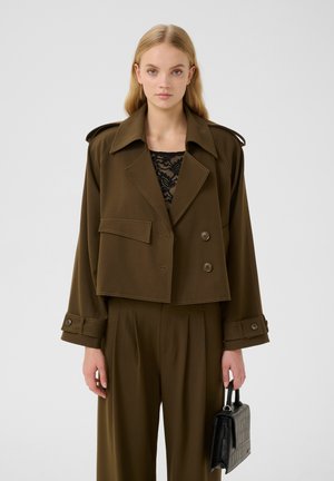 Olive green cropped jacket with double-breasted buttons, wide lapels, and subtle stitching. Paired with pleated pants and a black handbag.