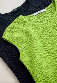 Deux hauts sans manches texturés, l'un vert citron et l'autre bleu marine, tous deux avec des encolures rondes et des étiquettes de la marque "NEXT".