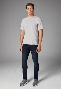Camiseta de manga corta gris claro, vaqueros ajustados azul oscuro y zapatillas grises. El fondo es de un gris neutro. Diseño simple, sin patrones.