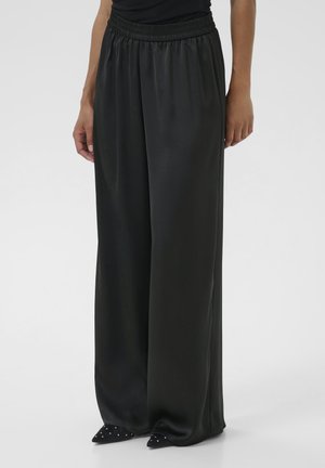 Black wide-leg satin pants with gathered elastic waistband worn with black pointed shoes studded with small silver embellishments.