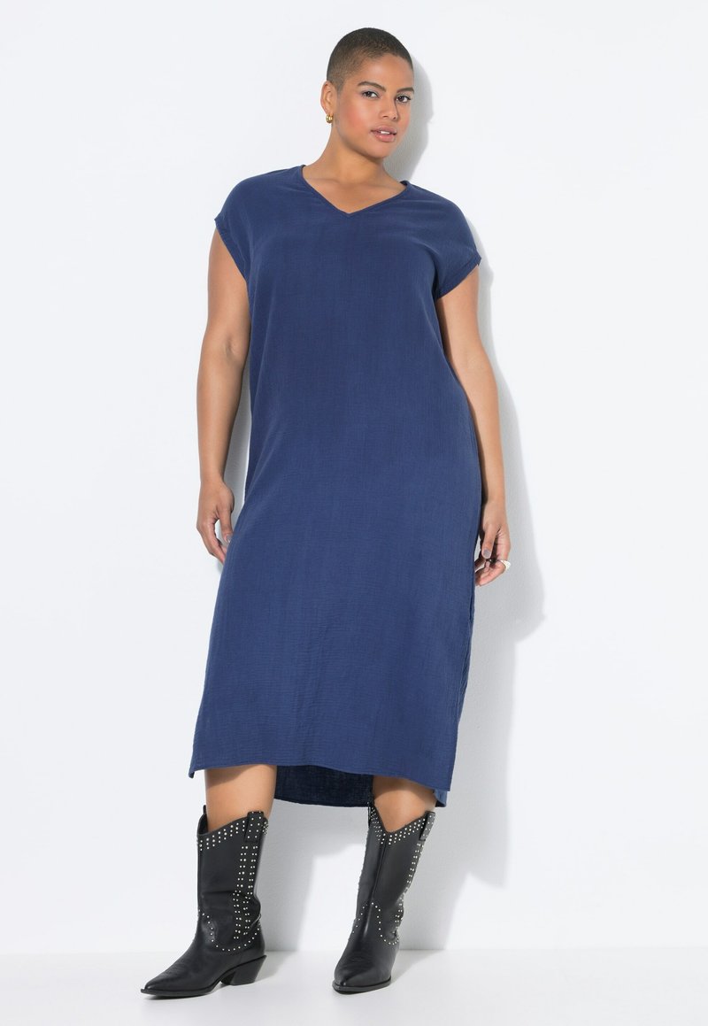 Marineblaues, knielanges, lässig geschnittenes Kleid mit kurzen Ärmeln und V-Ausschnitt. Getragen mit schwarzen, mit Nieten besetzten Cowboy-Stiefeln. Weiche Textur.