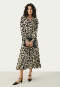 Robe imprimée léopard avec des manches longues et un col boutonné. Fabriquée en tissu léger, elle présente un ourlet évasé et une pochette noire.