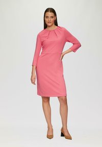 Rosa knielanges Kleid mit Dreiviertelärmeln, rundem Ausschnitt und gefaltetem Detail an der Vorderseite. Glatter Stoff, figurbetonte Silhouette.