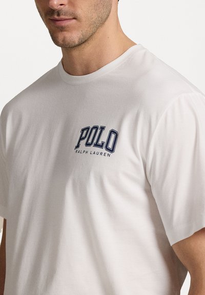 Balta medvilninė marškinėliai su trumpomis rankovėmis, ant krūtinės turintys tamsiai mėlyną siuvinėtą "POLO RALPH LAUREN" logotipą. Lygi tekstūra.