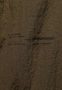 Brunt stof med en krøllet tekstur, der viser trykte sorte specifikationer og branding for 23ENGINEERED. Synlige detaljer inkluderer monteringskoder.