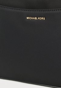 Bolsa negra de nailon con superficie texturizada y logotipo dorado "MICHAEL KORS". Diseño sencillo, sin patrones ni adornos adicionales.