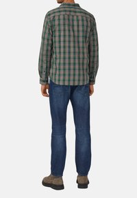 Camisa de cuadros verde y azul con mangas largas, cuello abotonado y diseño en la parte posterior, combinada con jeans azules y botas marrones hasta el tobillo.