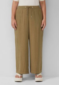 Pantalons larges kaki avec une taille élastique et un cordon de serrage. Le tissu semble léger et texturé. Portés avec des chaussures à plateforme.