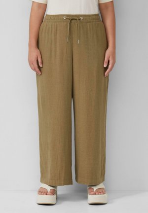 Pantalons larges kaki avec une taille élastique et un cordon de serrage. Le tissu semble léger et texturé. Portés avec des chaussures à plateforme.