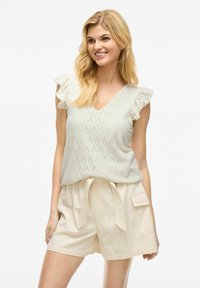 Lys grøn, ærmeløs top med blonderdetaljer og flæser på skuldrene, parret med beige shorts med snoretræk og sidelommer.