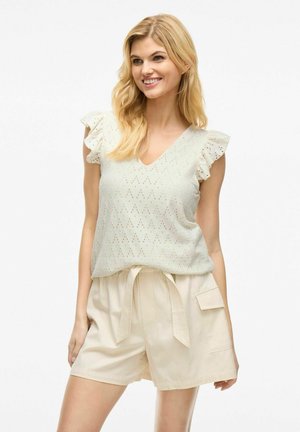 Haut sans manches vert clair avec des détails en dentelle et des épaules volantées, associé à un short beige à cordon de serrage avec poches latérales.
