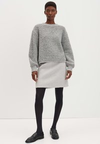 Grijze, gestructureerde trui met een losse pasvorm en lange mouwen, gecombineerd met een aansluitende grijze rok en zwarte panty's. Zwarte instappers maken de look compleet.