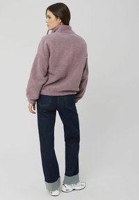 Veste en polaire lavande duveteuse avec un col montant, coupe décontractée et poignets côtelés, associée à un jean en denim bleu marine avec ourlets retroussés.