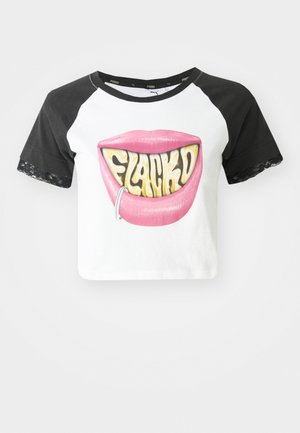 Top corto con mangas raglán negras, cuerpo blanco, con un gran gráfico de labios rosas con el texto "FLACKD" y un aro de labio plateado. Acentos de encaje en las mangas.