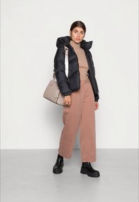 Must musta jakk, beež kudumisvillane, pehmed roosad laiad püksid ja mustad paksud saapad; kannab halli käekotti, millel on õla rihm.