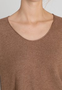 Braun gestricktes Oberteil mit weitem Rundhalsausschnitt und weicher Textur. Der Stoff hat eine feine Webart, die ihm ein lässiges Aussehen verleiht.