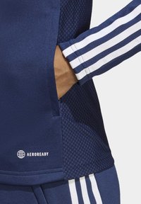 Navy Sporttop mit strukturierten Einsätzen, weißen drei Streifen an den Ärmeln und Aeroready-Logo nahe dem Saum.