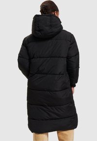 Černý zateplený kabát, délky po kolena, má kapuci, horizontálně prošívanou texturu a volný střih. Bez viditelných zapínání či dalších akcentů.