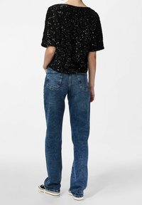 Top corto a maniche corte in paillettes nere abbinato a jeans in denim blu, con una vestibilità rilassata e gambe dritta. I dettagli includono cuciture a contrasto e tasche.