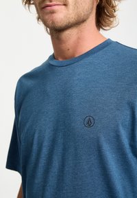 Blå T-shirt med korte ærmer lavet af blødt stof. Har en rund halsudskæring og et lille sort logo på brystet. Subtil tekstur.