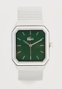 Ασημένιο ρολόι χειρός Lacoste με πράσινο ορθογώνιο καντράν, μινιμαλιστικούς δείκτες ώρας, τρία δείκτες και μεταλλικό λουράκι με οριζόντιες αυλακώσεις.