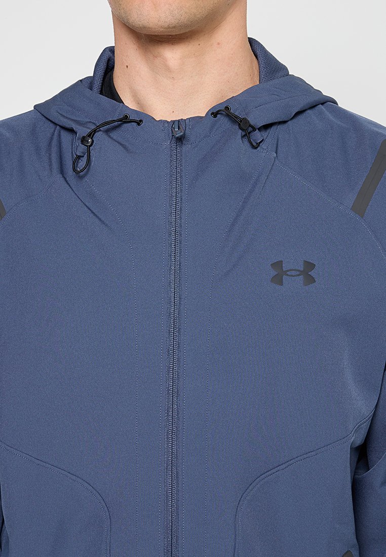 Veste à zip bleue marine avec capuche, en tissu lisse, dotée d'accents noirs et d'attaches réglables sur la capuche.