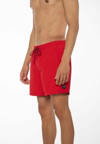 Costumi da bagno rossi con elastico in vita e cordoncino, dotati di un piccolo logo nero sul lato e realizzati in un tessuto liscio e leggero.