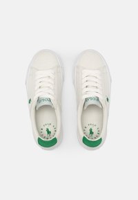 Zapatillas de lona beige con acentos verdes, lazadas blancas y un logo en el lateral y en la plantilla. Punta redondeada y suela texturizada.